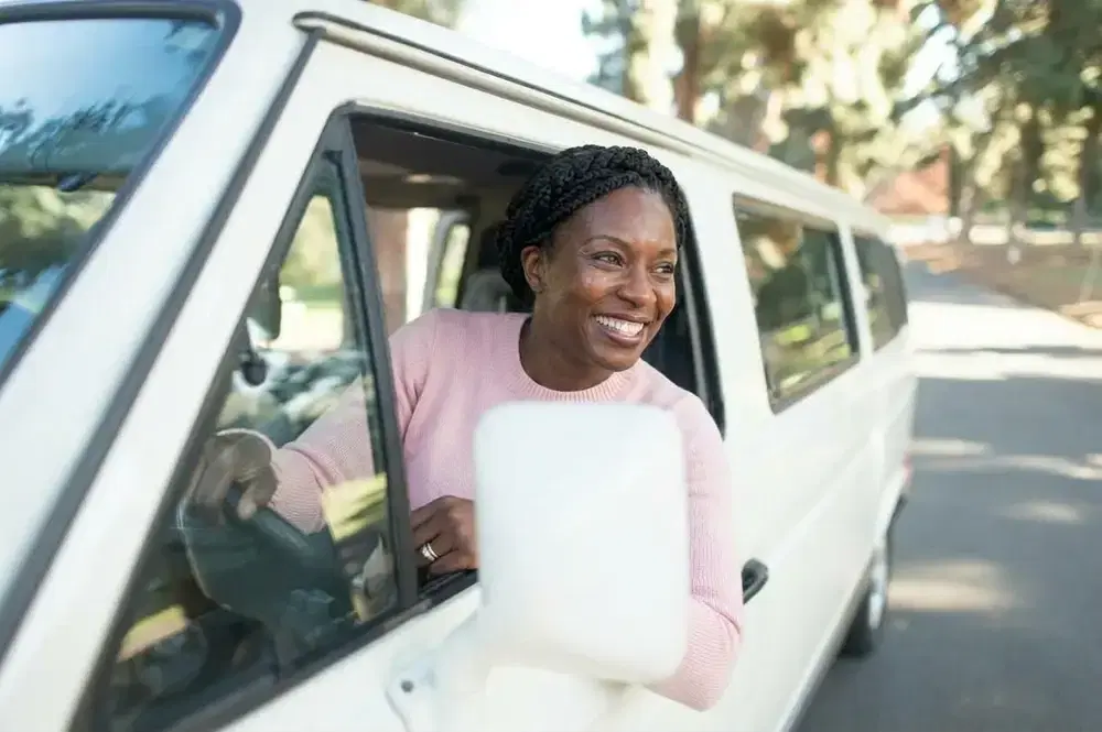 Conductrice souriante au volant, penchée à la fenêtre de son véhicule